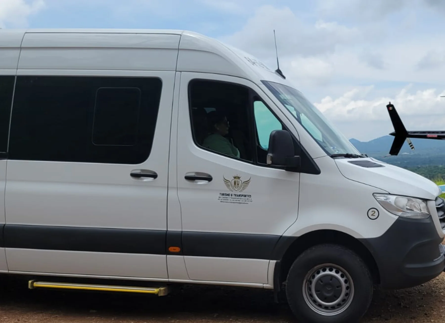 Camioneta Sprinter de MH Turismo & Transportes con el escudo de la empresa en la puerta, durante un servicio turístico en un mirador